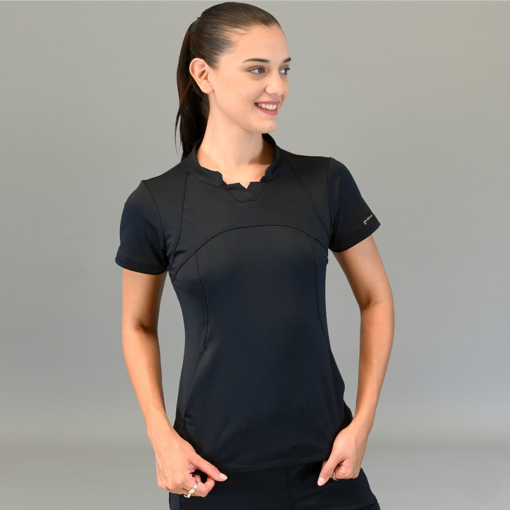 Model wearing Women's Top 910 black super stretch scrubs looking to the side with hands near hips.