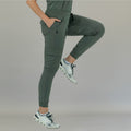 Woman posing with one leg raised, wearing jasper green 910 super stretch jogger pants.